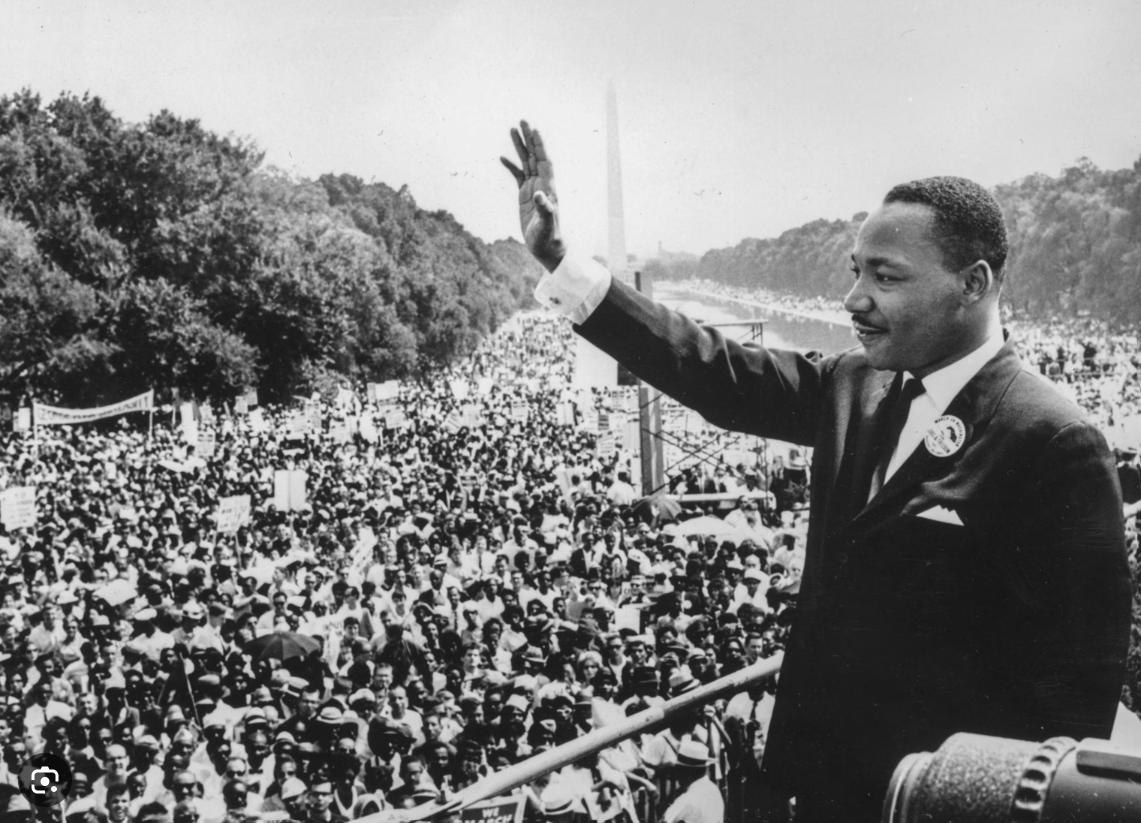Dr. Martin Luther King Jr. waving to a large audience in black and white. 